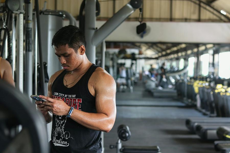 Un hombre mirando su celular de pie en medio de un gimnasio