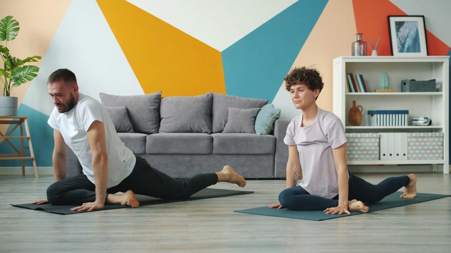 Pareja haciendo posturas de yoga sobre mats en el living