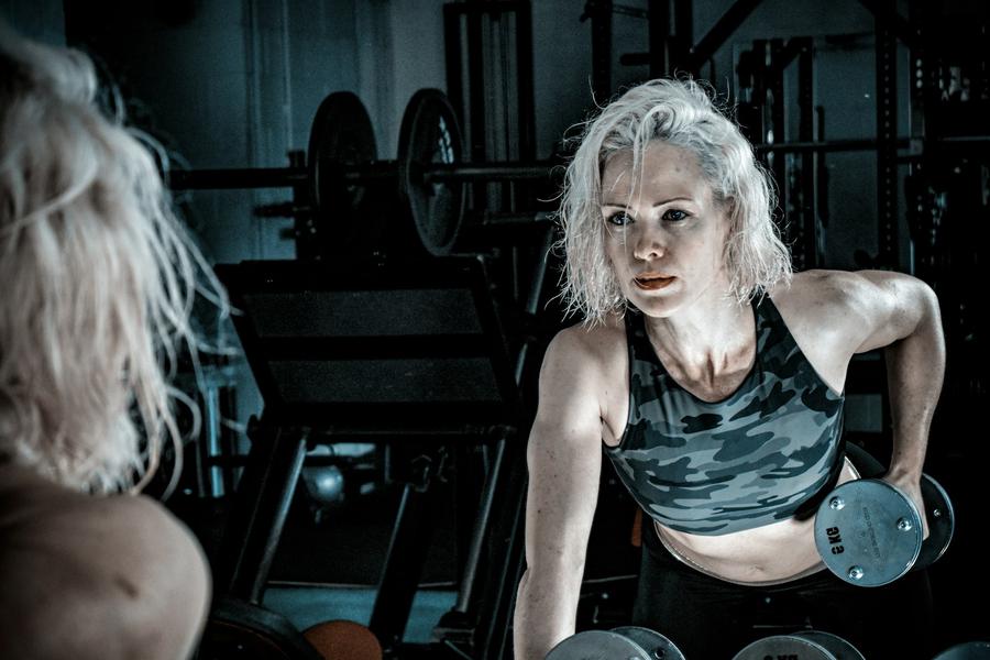 Mujer de pelo canoso entrenando con una mancuerna frente al espejo de una sala de fuerza