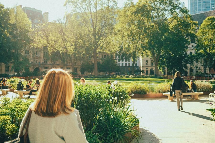 Mujer caminando por un parque soleado con gente relajándose