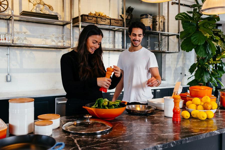 Hombre y mujer de pie frente a una mesa cocinando