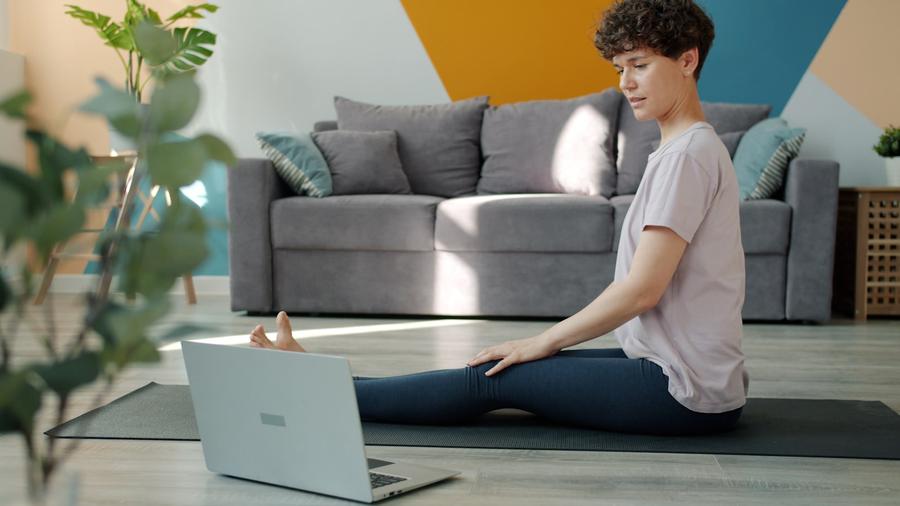 Mujer estirando en un mat de yoga mirando la laptop