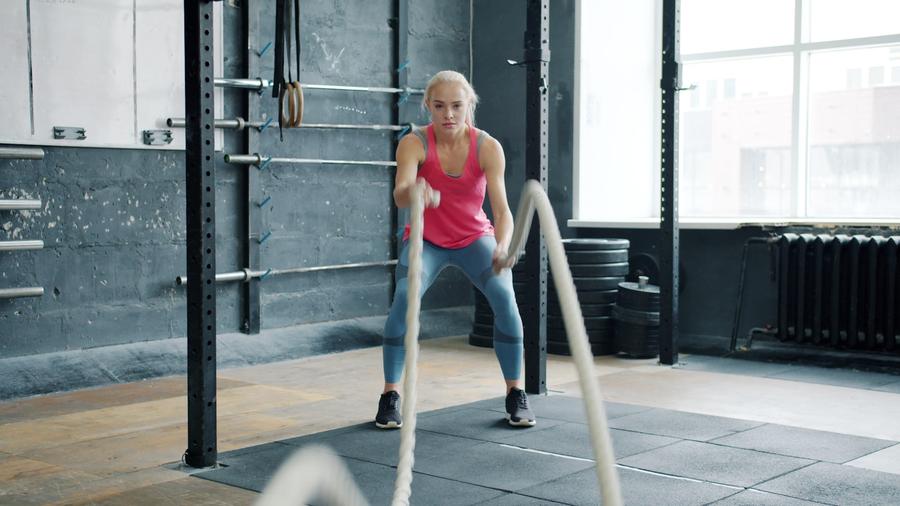 Mujer entrenando con cuerdas de batalla en el gimnasio