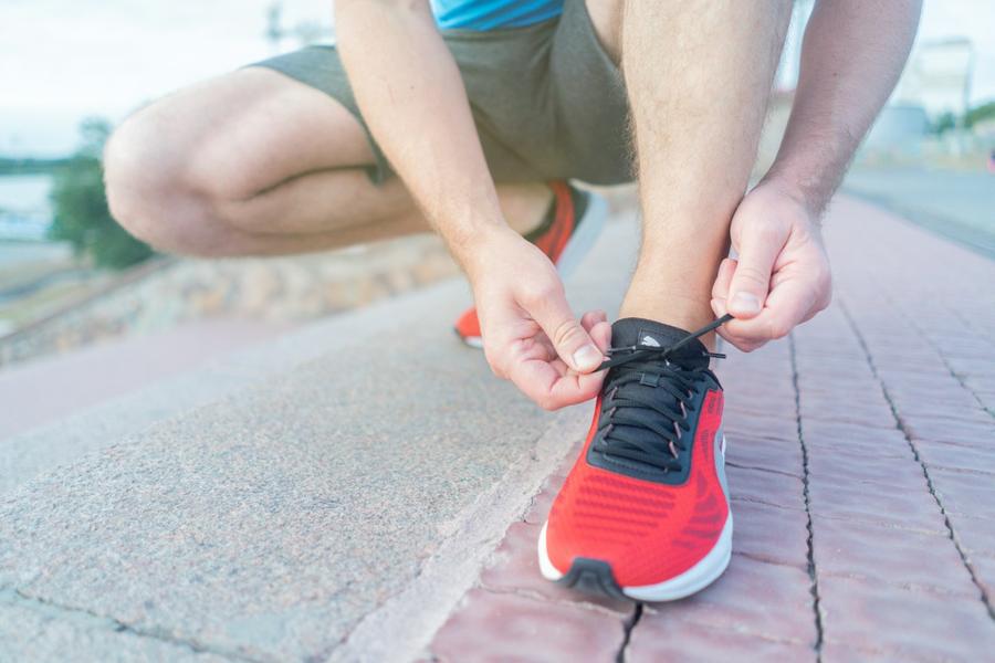 Una persona agachada atándose los cordones de la zapatilla antes de salir a entrenar